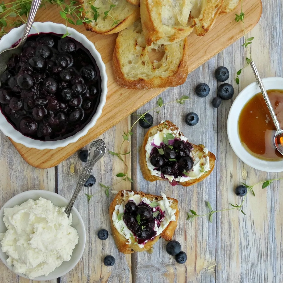 Ready to serve Blueberry and Goat Cheese Crostini Appetizers along with a bowl of blueberry sauce, honey and toasted slices of baguette