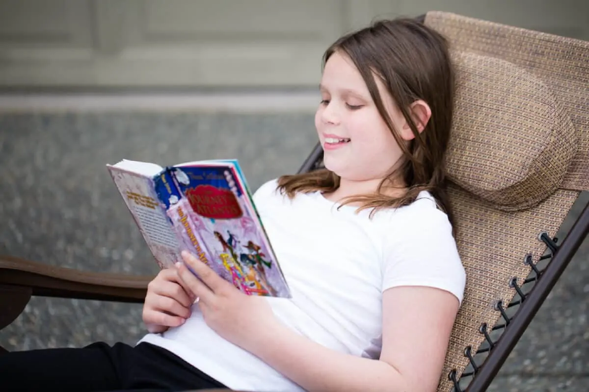 girl reading a book outside on a lawn chair