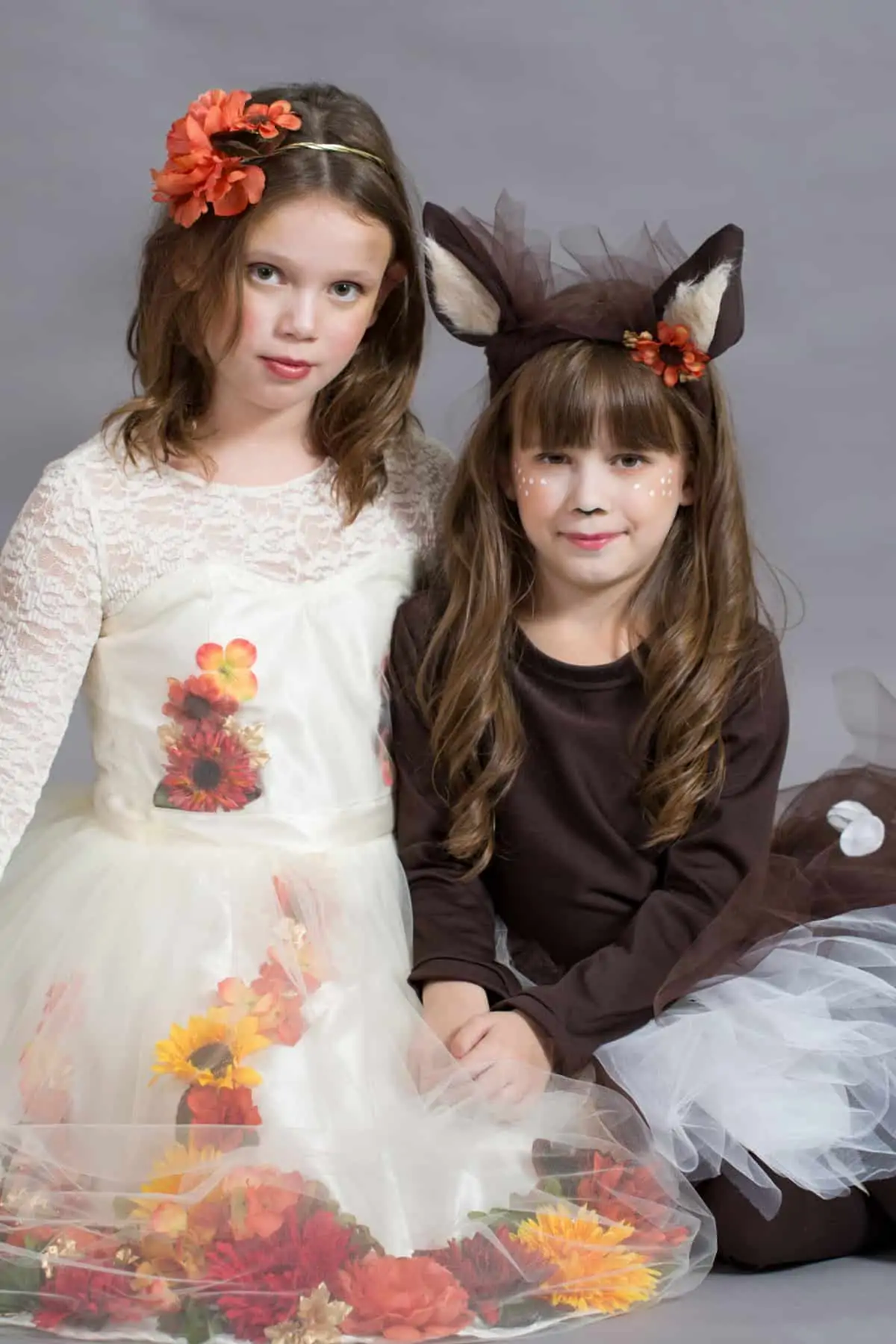 Two young girls dressed in pretty handmade costumes. The first girl is dressed in a white dress with fall flowers and the second girl is dressed as a fawn.