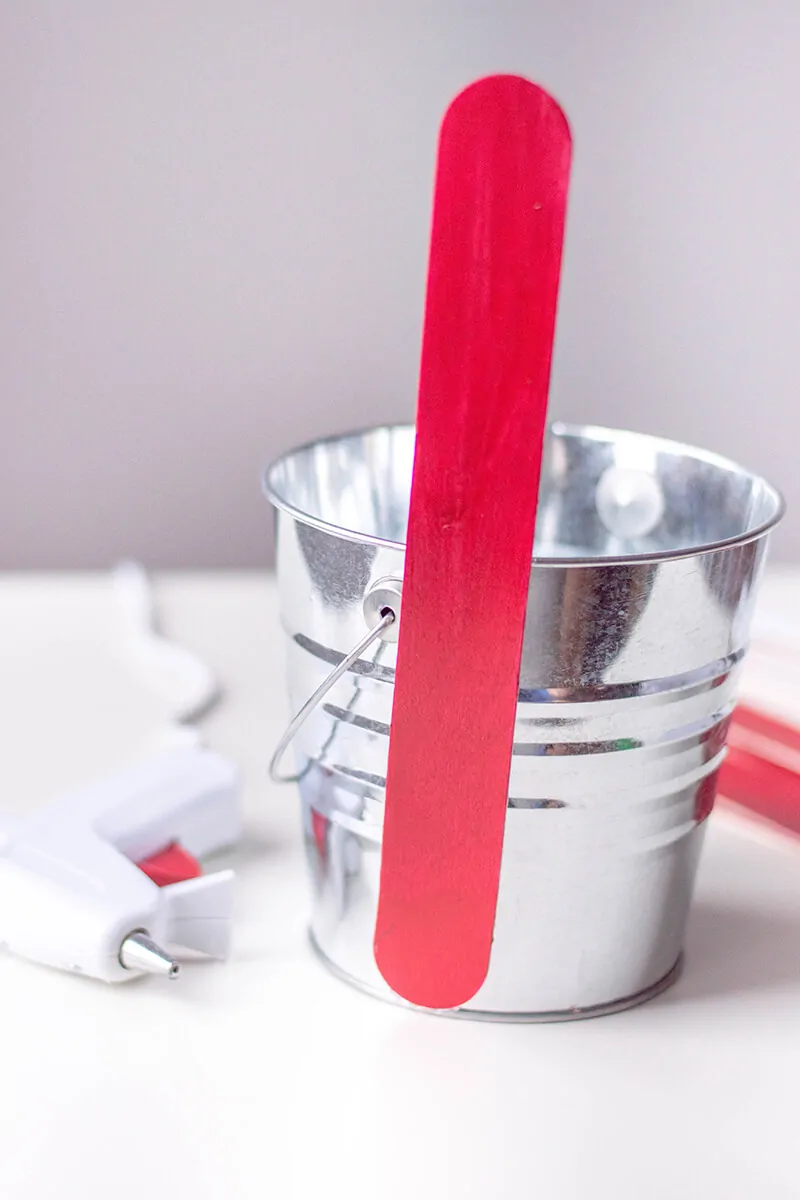 Attaching large red craft stick to metal pot.