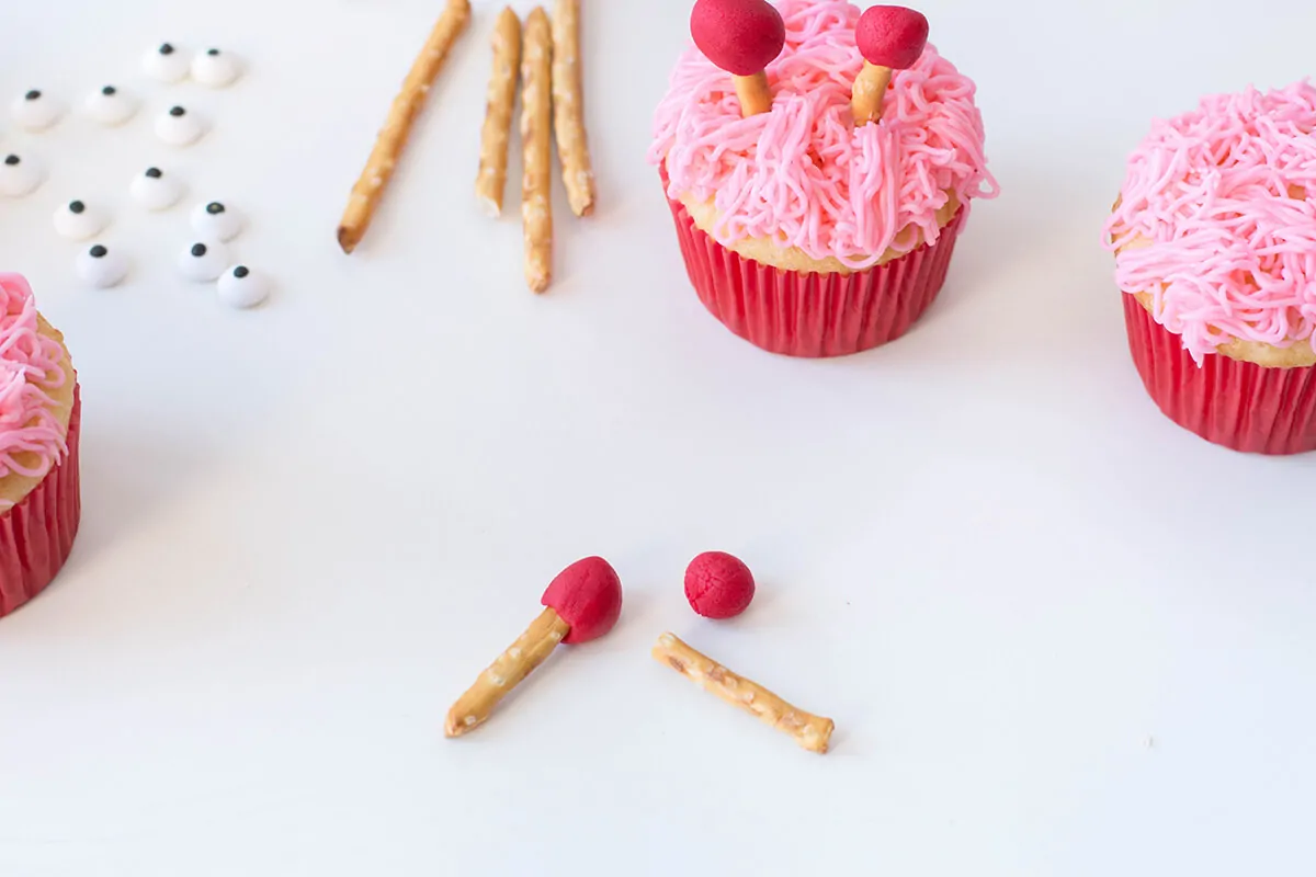 Decorating cupcakes with candy eyes and pretzels.