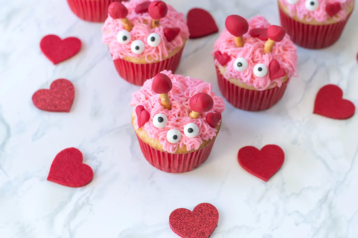 Pink and red decorated Valentines cupcakes sitting on a marble counter with heart decorations.