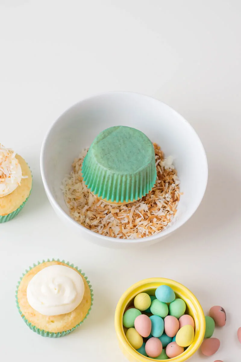 Adding coconut topping to vanilla cupcakes to make Bird's Nest Cupcakes.