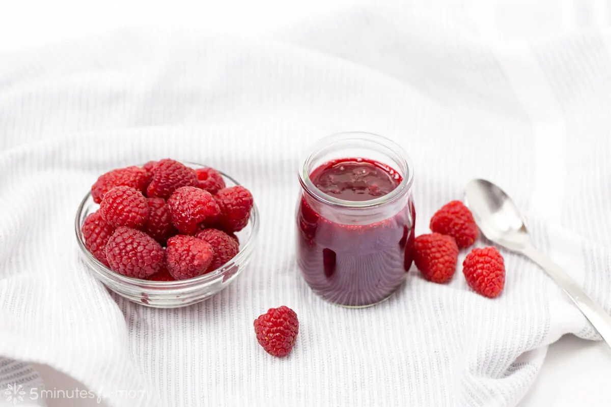 Jar of homemade Raspberry Coulis next to a bowl of fresh raspberries