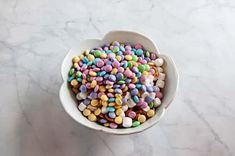 spring snack mix ingredients in clear bowls, and white bowl on white marble background