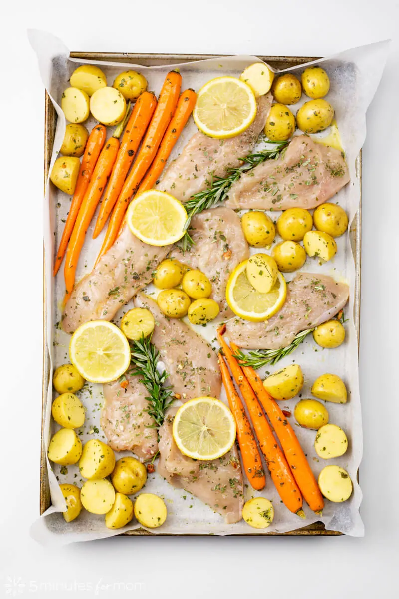 Lay out seasoned raw chicken and vegetables on baking pan