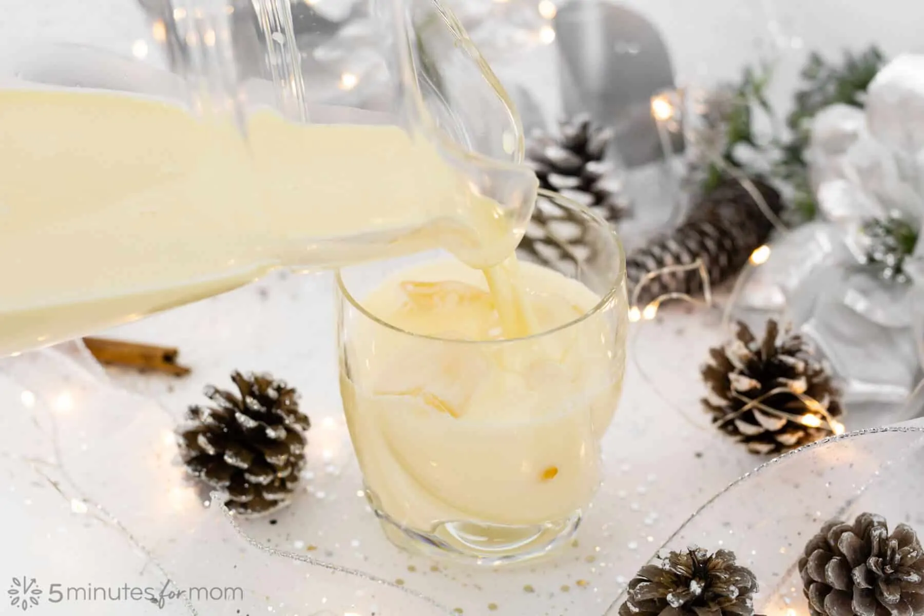 pouring cooked eggnog into a glass with silver holiday decorations on the table