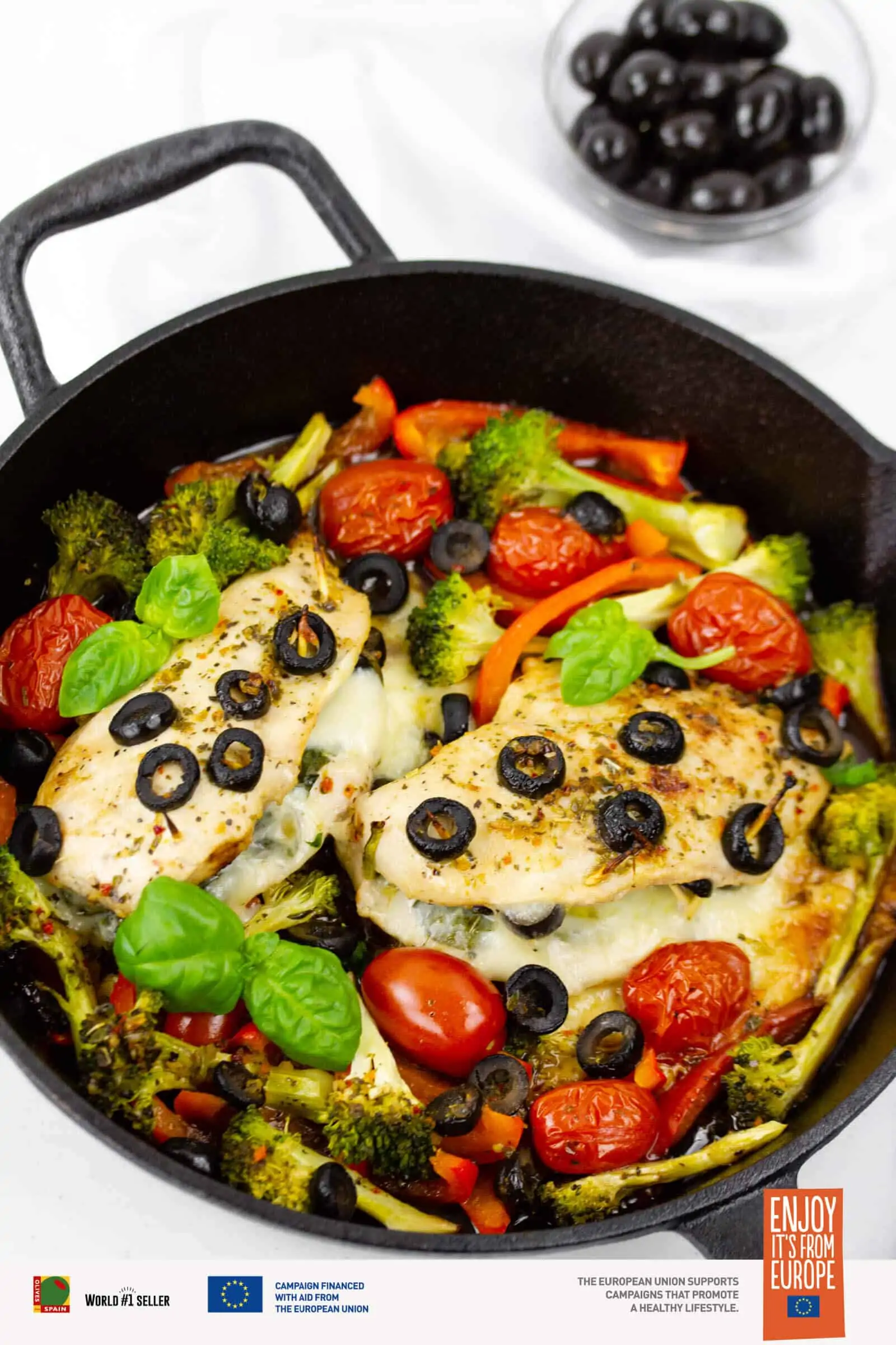 Stuffed chicken breasts with olives, tomatoes, and basil cooked in a cast iron pan.