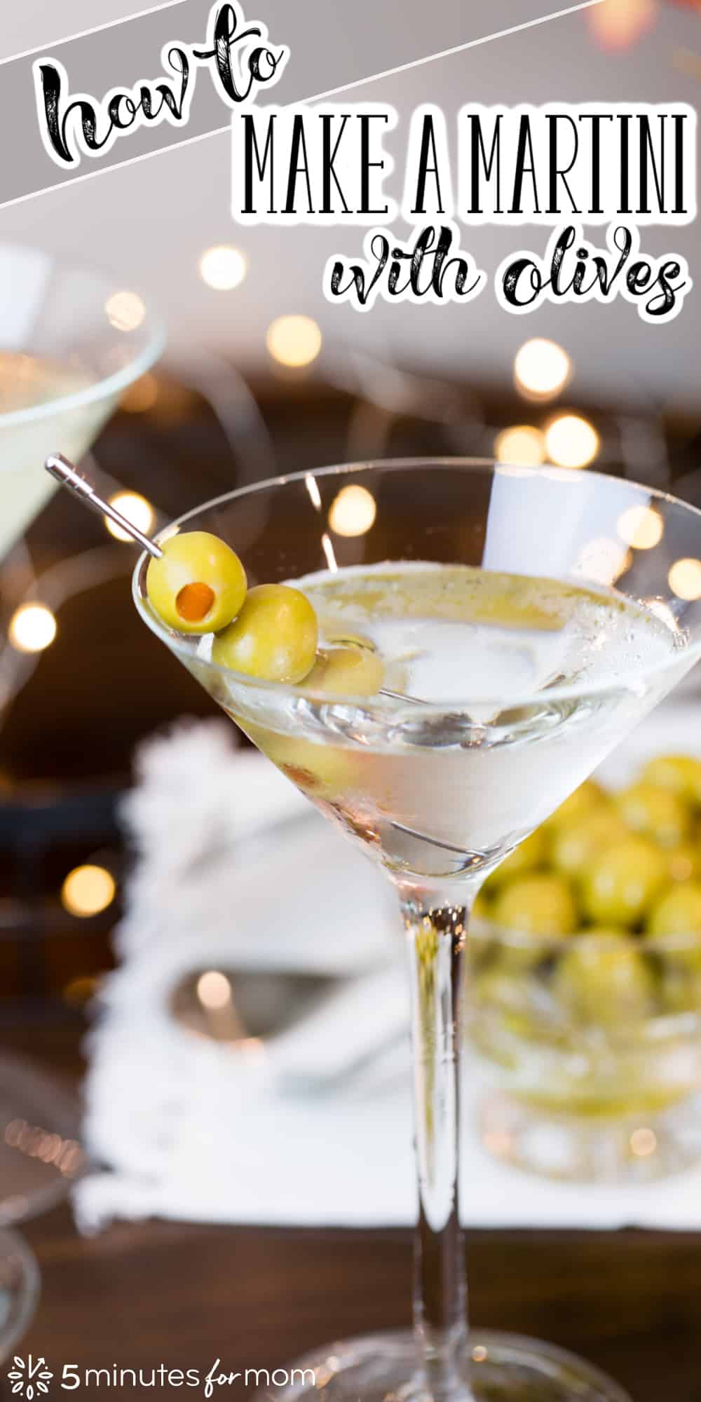Martini glass with dry martini and 3 olives on a skewer. In the background is a wooden serving tray with a glass bowl of olives. Text on image says "How To Make a Martini with Olives"