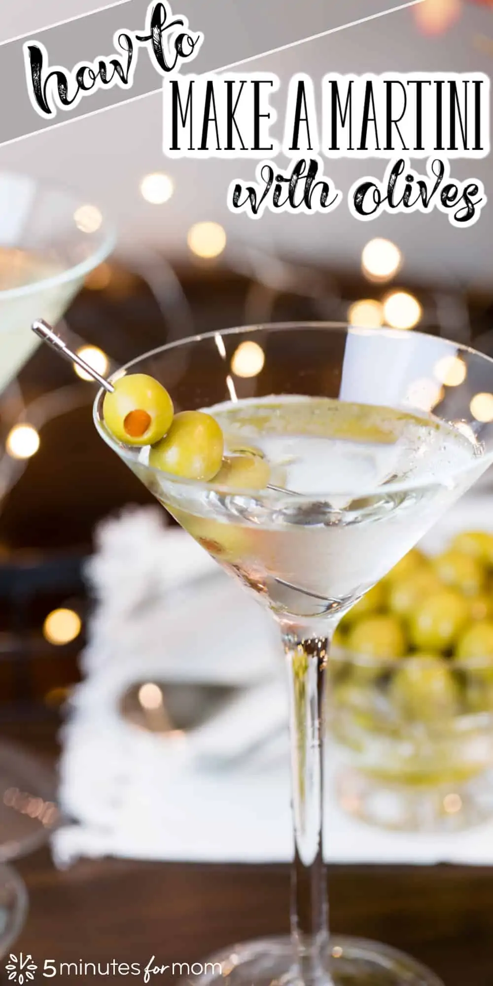 Martini glass with dry martini and 3 olives on a skewer. In the background is a wooden serving tray with a glass bowl of olives. Text on image says "How To Make a Martini with Olives"