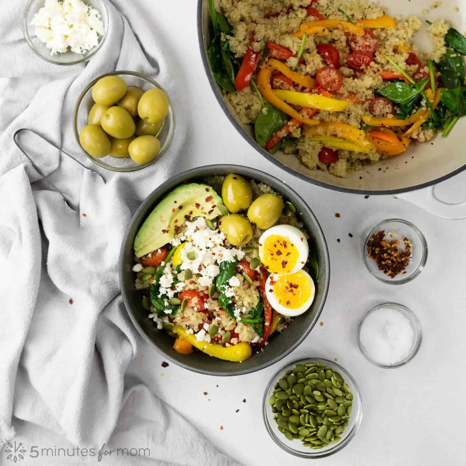 a Dutch oven with sautéed vegetables and quinoa next to a bowl of quinoa, vegetables, soft-boiled egg, avocado and green olives