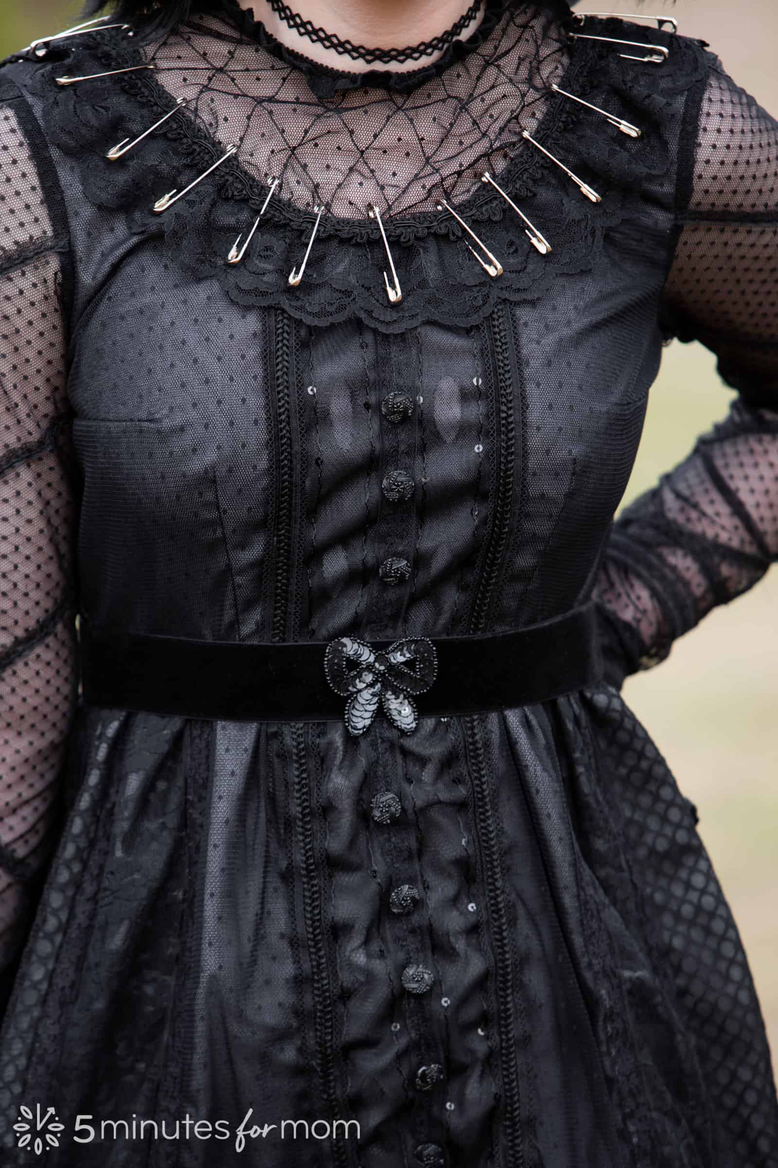 Close up view of the black dress worn by Lydia Deetz in Beetlejuice showing details of stitching, the variety of lace and black fabrics and safety pins. 