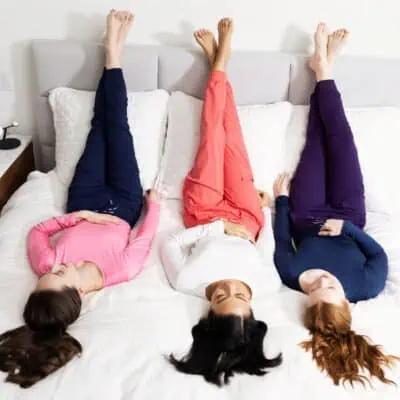 Showing a gift idea for women - Three women wearing colorful scrubs including long sleeve shirts and joggers on a bed